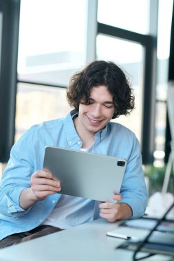 Yakışıklı bir adam şık, doğal ışıklandırılmış bir ofiste tablete gülümsüyor..