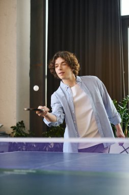 Genç yakışıklı bir adam şık bir ofiste yeteneklerini sergileyerek canlı bir masa tenisi oynamaktan hoşlanıyor..