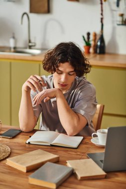 İyi görünümlü genç bir adam modern bir çalışma alanında otururken not defteriyle düşünceli bir şekilde meşgul olur..