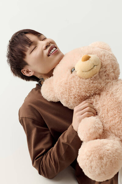 Молодой красивый азиатский мужчина радостно улыбается, обнимая пушистого плюшевого медведя в теплой атмосфере.