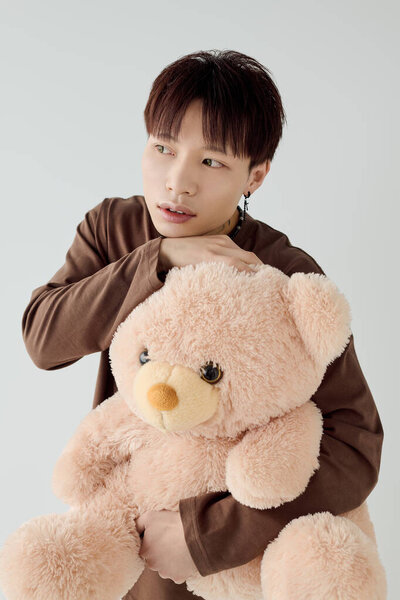 Молодой человек держит пушистого плюшевого мишку, источая тепло и очарование в спокойной обстановке.