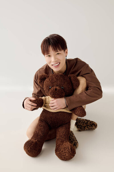 Молодой азиат радостно улыбается, обнимая мягкого плюшевого мишку в игровой момент.