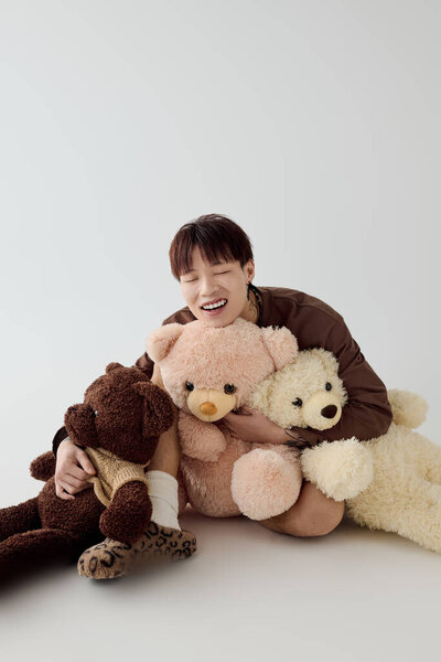 Веселый молодой человек обнимает трех милых плюшевых мишек на мягком, теплом фоне.