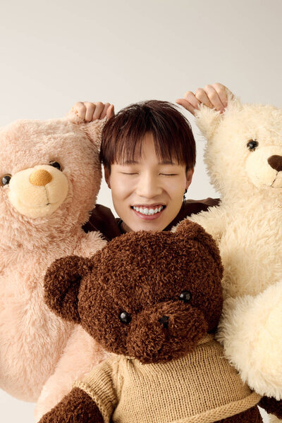 Радостный молодой человек улыбается, обнимая милых плюшевых мишек на светлом фоне.