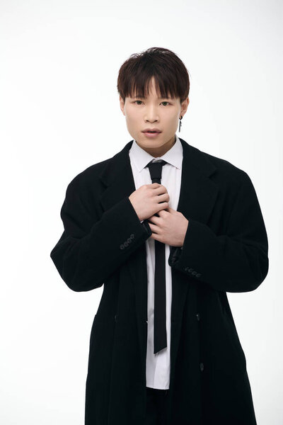 A well groomed young Asian man confidently adjusts his tie in a stylish coat.
