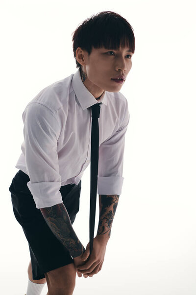 A handsome young Asian man in a white shirt and black shorts ties his necktie confidently.