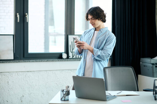 A good looking young man stands in a stylish office, interacting with his smartphone while working.