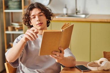 Yakışıklı genç bir adam ahşap bir masada oturuyor, çağdaş ofis ortamındaki bir kitaba odaklanmış..