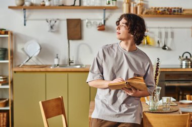 Genç bir adam şık ofisinde durup düşünceli bir şekilde bir kitap okuyor..