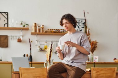 Kıvırcık saçlı genç adam kahvesini yudumlarken ve şık bir ofiste işine odaklanırken rahatlıyor..