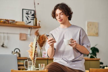 Genç yakışıklı adam şık bir ofis ortamında kahve ve telefonla rahatlıyor..