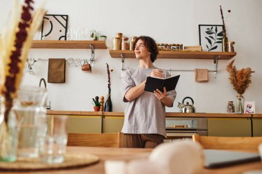 Genç ve yakışıklı bir adam modern bir ofiste duruyor ve fikirlerini defterine yazıyor..