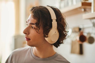 Kıvırcık saçlı yakışıklı genç adam şık bir ofis ortamında çalışırken müzik dinliyor..