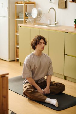 Genç ve çekici bir adam bir paspasın üzerinde bacak bacak üstüne atarak dinlendirici bir ofiste meditasyon yapıyor..