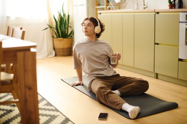 Yakışıklı genç adam müzik dinlerken ve su içerken yoga minderinde vakit geçirmekten hoşlanıyor..