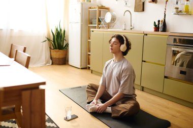 Genç bir adam, modaya uygun bir ofiste yoga minderinin üzerinde bacak bacak bacak üstüne atıyor..