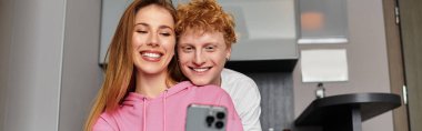 A young couple shares a loving moment while taking a selfie together in their hotel room. clipart