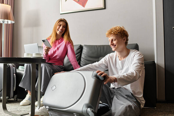 A young couple enjoys joyful moments in a stylish hotel room, bonding over their travels.