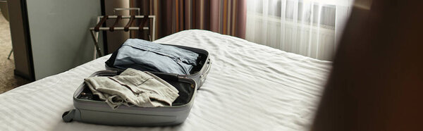 Comfy well lit hotel room with a bed and packed luggage.