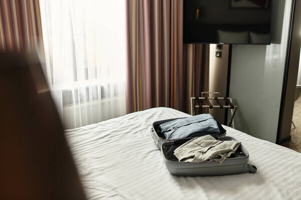 Cozy hotel room with a bed and packed luggage, white and brown curtains.