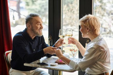 Orta yaşlı bir çift, samimi bir randevunun keyfini çıkarırken kadehlerini kadehleriyle ve kahkahalarını paylaşır..