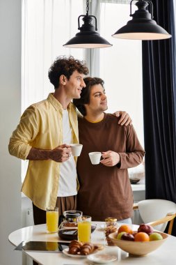 Şık bir dairede, iki erkek sıcak bir kahvaltıdan zevk alır, gülümseme ve sıcaklığı paylaşırlar..