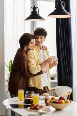 İki adam şık bir dairede sıcak bir anı paylaşıyor, kahvaltı ve kahkahalarla eğleniyorlar..