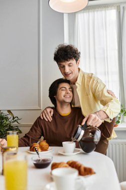 Eşcinsel çift, rahat evlerinde keyifli bir anı paylaşırken kahve akıyor ve gülümsüyor..