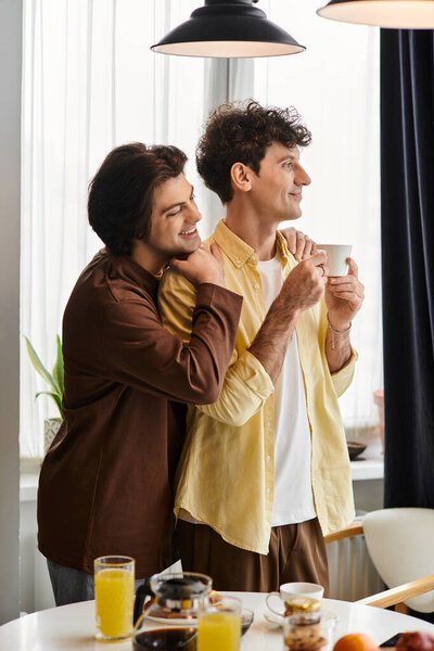 гей-пара счастливо обнимается в своей стильной квартире, наслаждаясь вместе завтраком.