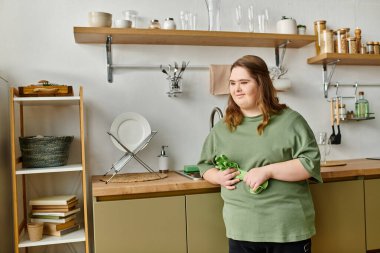 Down sendromlu genç bir kadın mutfaktaki yeşil mutfak aletini tutarken gülümsüyor..