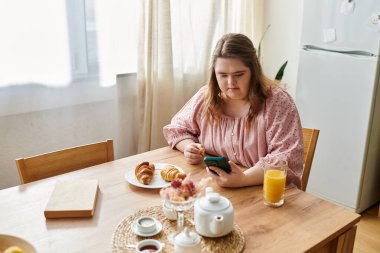 Sakin bir mutfakta, Down sendromlu genç bir kadın akıllı telefonuyla rahatlıyor..