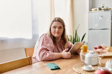 Down sendromlu kendinden emin genç bir kadın masada oturup tabletinin ve içkisinin tadını çıkarıyor..