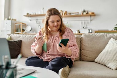Down sendromlu kendine güvenen genç bir kadın telefonunu ve defterini kullanarak evde rahatlıyor..