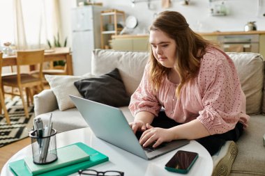 Down sendromlu genç bir kadın evde oturup laptopuyla uğraşıyor..