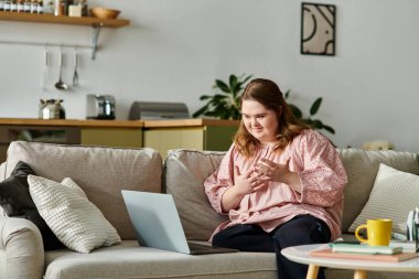 Genç ve güzel bir kadın evdeki kanepede rahatça oturur ve dizüstü bilgisayarıyla mutlu mesut meşgul olur..