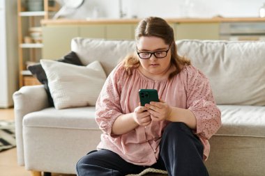 Rahat bir oturma odasında, Down sendromlu genç bir kadın güvenli bir şekilde akıllı telefonunu kullanıyor..