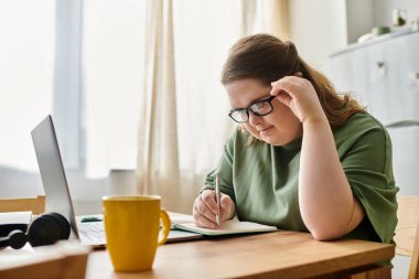 Sıcak atmosfer, Down sendromlu genç bir kadının deftere yazmaya odaklanmasını yansıtıyor..