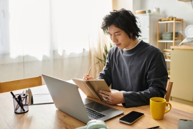 Yakışıklı genç bir adam online çalışmalar yapıyor, evde dizüstü bilgisayar kullanırken notlar alıyor..