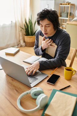 Evde, genç Asyalı bir öğrenci dizüstü bilgisayar kullanarak ve kahvesini yudumlayarak online çalışmaya odaklanıyor..