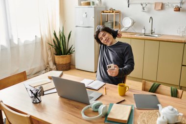 Tahta bir masada oturan genç bir adam internetten bilgisayarla ders çalışıyor ve notlar alıyor..