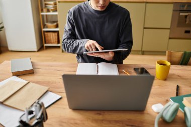 Odaklanmış öğrenci, evde sanal öğrenme faaliyetlerinde bulunmak için bir dizüstü bilgisayar ve tablet kullanır.