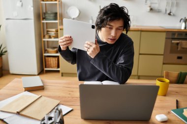 Yakışıklı Asyalı öğrenci ahşap bir masada otururken online çalışmalarına odaklanıyor..