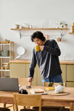 Şık bir genç adam evinde laptopuyla çalışırken sıcak bir içkiden zevk alır..
