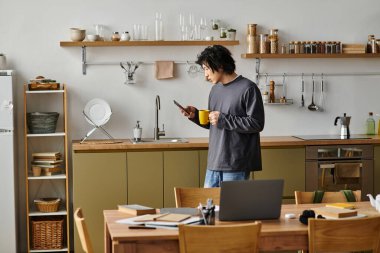 Bilgisayarı ve kahveyle çevrimiçi olarak ev mutfağında çalışan genç bir öğrenci..