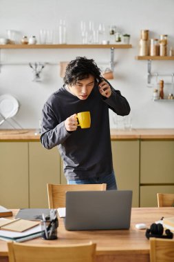 Bir öğrenci evde kahve yudumlarken ve telefonda konuşurken online çalışmalara odaklanır..