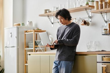 Genç bir Asyalı öğrenci dizüstü bilgisayarına yoğunlaşarak evden online eğitimin keyfini çıkarıyor..