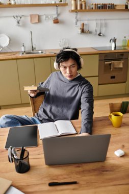 Yakışıklı genç bir adam evdeki çevrimiçi çalışmalarına odaklanıyor, rahat bir atmosferle çevrili..