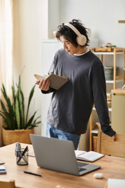 Evde yakışıklı genç bir öğrenci müzik dinlerken çevrimiçi çalışıyor ve öğrenmeye odaklanıyor.