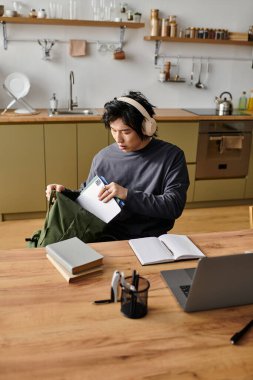 Genç bir adam evinde internetten öğrenim görüyor, derslerine odaklanıyor ve etrafı kitaplarla çevrili..