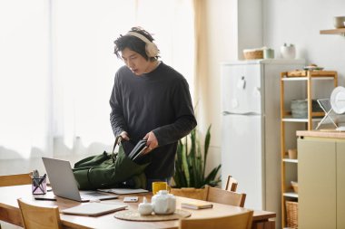 Yakışıklı genç adam evde online derslere hazırlanırken çantasının fermuarını çeker..
